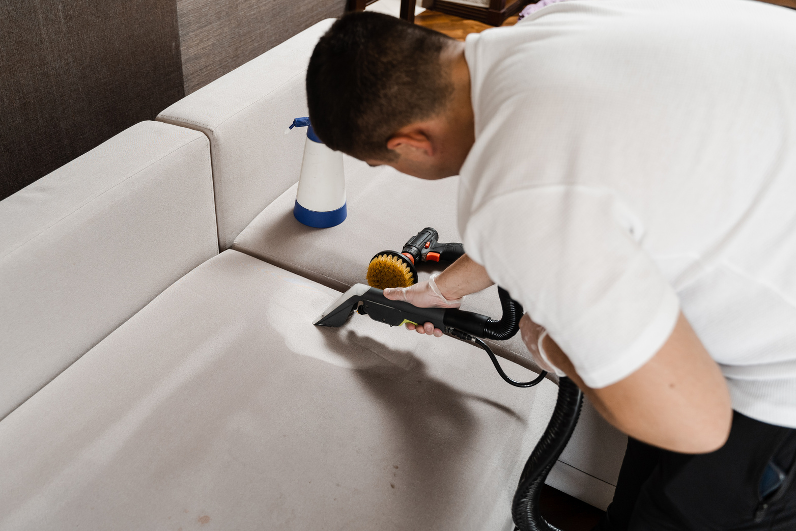 Housekeeper is extracting dirt from upholstered sofa using dry cleaning extraction machine. Cleaner is cleaning couch with washing vacuum cleaner extractor machine for dry clean upholstered furniture.
